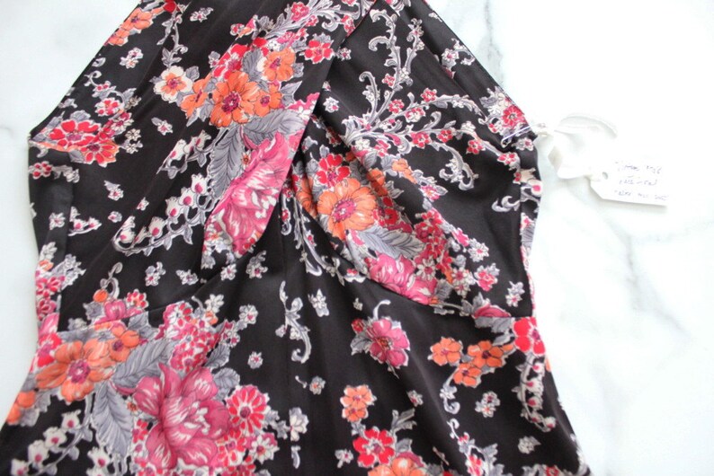 May include: A black dress with a floral print featuring pink, orange, and grey flowers. The dress has a V-neckline and a gathered detail at the bust.