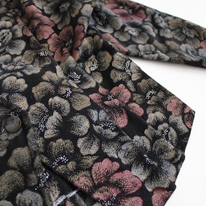 May include: A black cardigan with a floral pattern in shades of pink, gray, and gold. The cardigan has a button closure and a long sleeve.