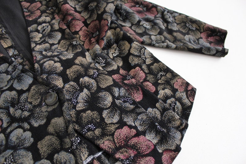 May include: A black cardigan with a floral pattern in shades of pink, gray, and gold. The cardigan has a button closure and a long sleeve.