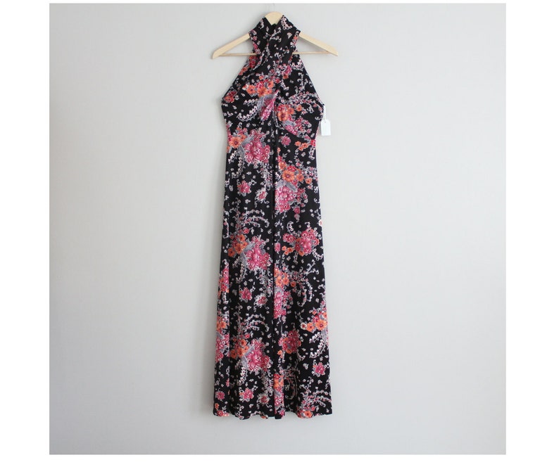 May include: A black maxi dress with a floral print in shades of pink, orange, and white. The dress has a halter neckline and a criss-cross design at the front.