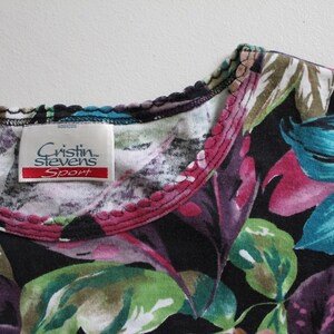 May include: Black floral print shirt with a pink and green trim around the neckline. The shirt has a label that reads "Cristin Stevens Sport".