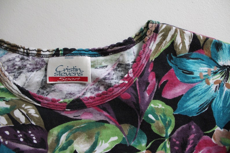 May include: Black floral print shirt with a pink and green trim around the neckline. The shirt has a label that reads "Cristin Stevens Sport".