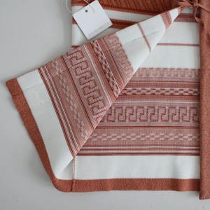 Op de afbeelding: Een wit en oranje gestreepte gebreide cardigan met een geometrisch patroon. De cardigan heeft een strik sluiting en is gemaakt van een zachte, comfortabele stof.