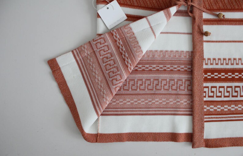 Op de afbeelding: Een wit en oranje gestreepte gebreide cardigan met een geometrisch patroon. De cardigan heeft een strik sluiting en is gemaakt van een zachte, comfortabele stof.