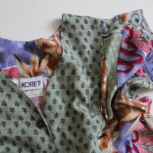 May include: A multi-colored, patterned dress with a V-neckline and short sleeves. The dress has a green, floral, and paisley print. The label on the dress reads "KORET".