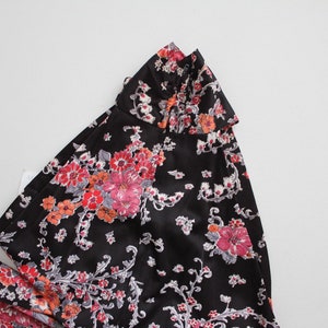 May include: A black dress with a floral print featuring pink, red, and white flowers. The dress has a ruffled collar.