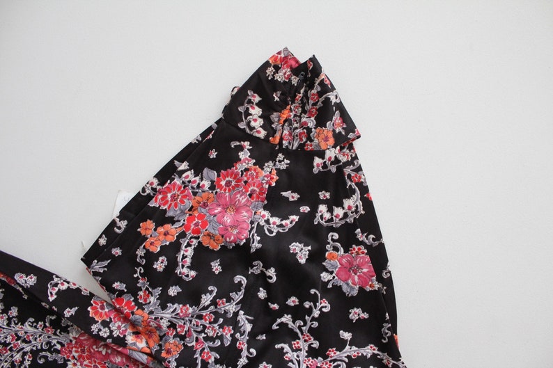 May include: A black dress with a floral print featuring pink, red, and white flowers. The dress has a ruffled collar.