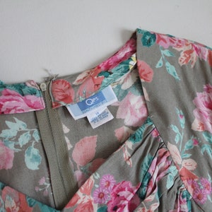 Op de afbeelding: Vintage jurk met een bloemenpatroon in roze, rood en teal op een grijze achtergrond. De jurk heeft een V-hals en een ritssluiting. Het label leest "Qps" en maat 12.