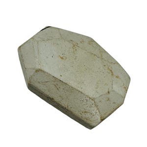 May include: A geometric, off-white, stone-like object with a faceted design. The object has a rectangular base and a multi-faceted top, with visible texture and subtle brown markings. The overall shape resembles a large gemstone.