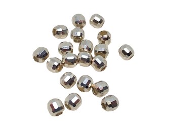 Può includere: Una collezione di piccole perline sfaccettate color argento sparse su uno sfondo bianco. Ogni perlina ha molteplici superfici piatte che riflettono la luce, creando un effetto scintillante. Queste perline sono adatte per la creazione di gioielli e progetti di artigianato.
