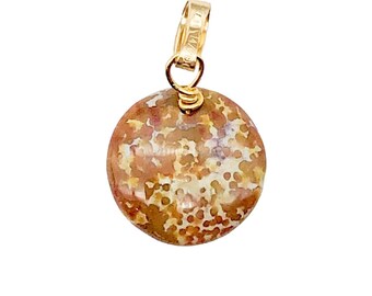 May include: A round pendant with a gold bail and wire wrap. The pendant features a speckled pattern in shades of brown, tan, and cream. The jewelry is likely a necklace pendant or charm.