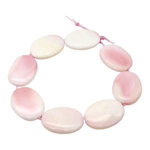 May include: A strand of oval-shaped beads in shades of pink and white, strung together with a pink cord. The beads have a smooth, polished surface, and the color gradient varies across each bead. The overall aesthetic is soft and feminine.