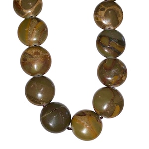 May include: A close-up of a necklace featuring large, round beads. The beads are primarily olive green with brown and tan marbling. The necklace is strung on a dark brown cord, creating a natural and earthy aesthetic.