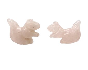 May include: Two rose quartz squirrel figurines. The squirrels are carved in a sitting position with their tails curved upwards. The color of the squirrels is a light pink. The background is white.