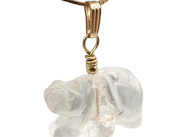May include: A clear quartz pendant in the shape of a bear, suspended from a gold-colored chain. The bear is intricately carved, showcasing its form. The pendant is attached to a gold-colored bail and wire wrap.