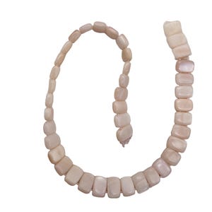 May include: A strand of light pink, rectangular beads. The beads are strung together, forming a curved shape against a white background. The beads have a smooth, polished appearance, and the color is a soft, natural hue.