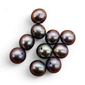 May include: A collection of dark brown, lustrous pearls, each with a unique iridescent sheen. The pearls are round, with visible drill holes, suggesting they are intended for stringing into jewelry. The arrangement is scattered against a white background.
