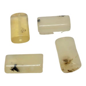 May include: Four translucent, off-white gemstone beads with dark inclusions. One bead is cylindrical, while the others are rectangular. The beads are likely for jewelry making or crafting.