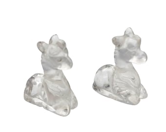 May include: Two clear quartz crystal figurines of a reclining deer. The deer are carved with detailed features, including antlers and a curved body. The figurines are set against a white background.
