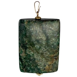 May include: A rectangular pendant with a mottled green and brown surface. The pendant has a gold-colored bail at the top and a small gold-colored accent at the bottom. The pendant is likely made of stone or a similar material.