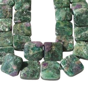 May include: A close-up of a strand of square-shaped beads. The beads are a mix of green and purple hues, with a marbled appearance. The beads are strung together, creating a necklace or bracelet.