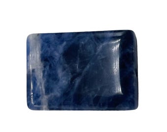 May include: A rectangular sodalite gemstone with rounded corners. The stone features a deep blue color with white marbling throughout, creating a unique pattern. The polished surface reflects light, highlighting the stone's natural beauty.