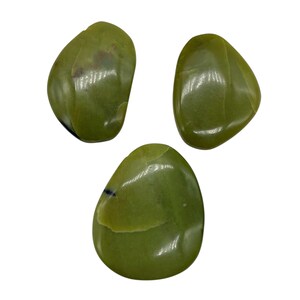 May include: Three smooth, polished green stones are displayed against a white background. The stones have a rounded, irregular shape and a glossy finish. The color is a muted, olive green with subtle variations in tone.