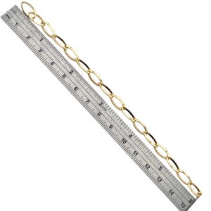 May include: A gold-colored chain with oval links, shown next to a ruler for scale. The chain is approximately 15 inches long, with the ruler providing precise measurements in inches and millimeters. The chain's design is simple and elegant.