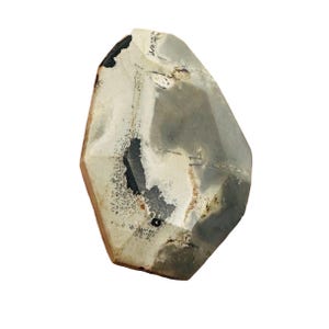 May include: A large, irregularly shaped stone with a light gray and white color palette. The stone features dark gray and black inclusions and a rough, textured surface. The edges are a light brown color. The stone appears to be a natural artifact.
