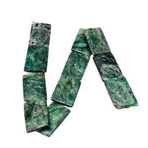 May include: A strand of rectangular green gemstone beads with dark green and purple inclusions. The beads are strung together with green thread, forming a decorative pattern. The gemstones have a polished, natural appearance.