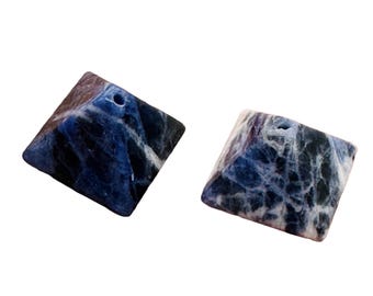 May include: Two square-shaped sodalite gemstones with a hole drilled through the top. The stones have a dark blue color with white veining and a polished finish. These gemstones are suitable for jewelry making.