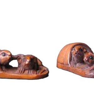 Puede incluir: Dos tallas de madera de animales pequeños. Una talla representa un conejo saliendo de un refugio, interactuando con otro animal. La segunda talla muestra dos animales dentro de un refugio. Ambos son marrones.