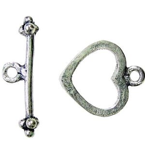 May include: A silver-toned toggle clasp set. The clasp features a bar with decorative ball accents and a heart-shaped loop. The metal has a textured, antique finish, suitable for jewelry making or craft projects.