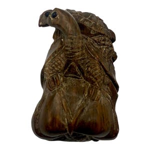 May include: A detailed, hand-carved wooden sculpture of a turtle. The sculpture is a rich brown color and features intricate details, including the turtle's head, shell, and legs. The turtle is depicted in a stylized, artistic manner.