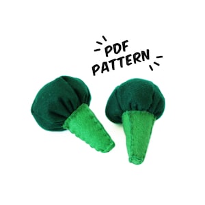 May include: Two green felt broccoli pieces with a PDF pattern text overlay. The broccoli pieces are made of felt and have a green stem.