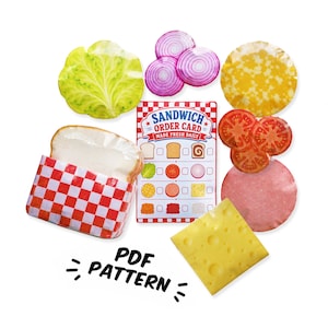 Könnte beinhalten: Ein Set aus Filz-Sandwich-Zutaten, bestehend aus einem Salatblatt, roten Zwiebelscheiben, einer gelben Käsescheibe, Tomatenscheiben, einer Schinkenscheibe, einem Stück Schweizer Käse und einer Brotscheibe in einer rot-weiß karierten Verpackung.