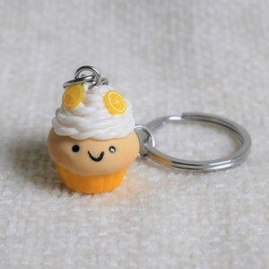Peut inclure: Un porte-clés en forme de cupcake avec un visage souriant, du glaçage blanc et des tranches de citron. La base est jaune et le porte-clés a un anneau argenté. Un accessoire charmant pour les amateurs de gourmandises.