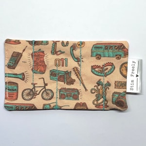 May include: A beige fabric pouch with a colorful print of various items, including a van, a bicycle, a walkie-talkie, a flashlight, a can, a cassette player, a clock, and a monster. The text "011" is printed on the pouch.