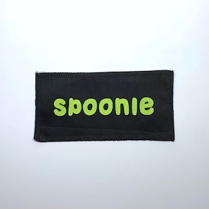 May include: Black fabric patch with the word "spoonie" in green lettering.