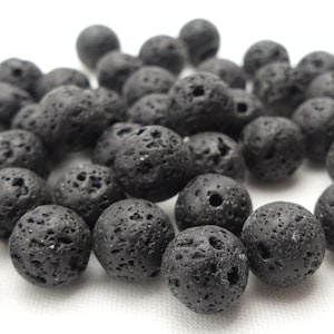 May include: A pile of black lava rock beads. The round beads have a porous, textured surface and vary in size. These beads are often used in jewellery making and other craft projects.
