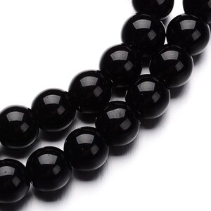May include: A strand of black gemstone beads, each bead is round and smooth. The beads are strung together on a clear thread.