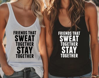 May include: Two tank tops, one white and one black, with the phrase "FRIENDS THAT SWEAT TOGETHER STAY TOGETHER" printed in bold, black and white letters. The tops are sleeveless and have a scoop neck design.