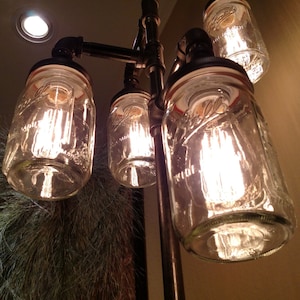 May include: A five-light industrial style lamp made from black metal pipes and clear glass mason jars. Each jar has a light bulb inside and is attached to the pipe with a metal ring. The lamp has a red valve at the bottom.