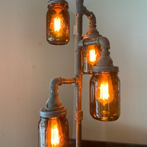 May include: A rustic industrial style floor lamp with four amber glass jars used as light fixtures. The lamp is made of black metal pipes and fittings.