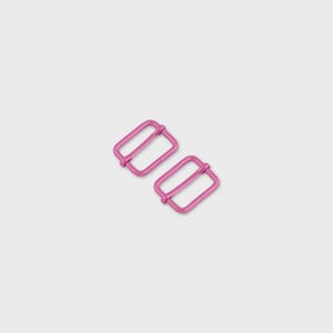 May include: Two pink metal rectangle sliders. These hardware pieces have a rectangular shape with a bar in the middle. The sliders are used for adjusting straps on bags, clothing, or other accessories.