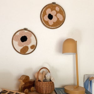 May include: Two circular wall hangings with pink and brown yarn flowers, a wicker basket with a stuffed bunny, a wooden toy duck, and a yellow table lamp on a table with a book.
