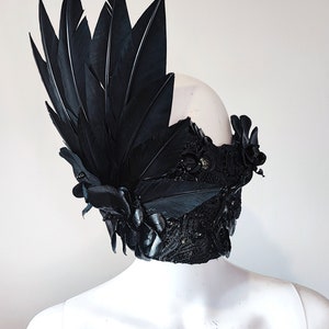 May include: A black masquerade mask with feathers and floral accents. The mask is made of lace and has a delicate, intricate design.