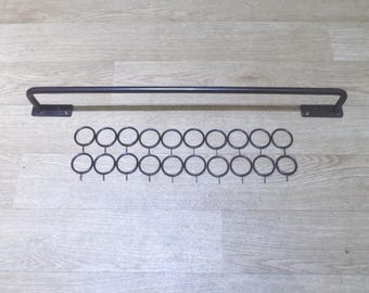 May include: A dark brown metal curtain rod with two flat mounting brackets at the ends, accompanied by a set of twenty matching circular curtain rings arranged in two horizontal rows, each featuring a small hook at the bottom for fabric attachment.