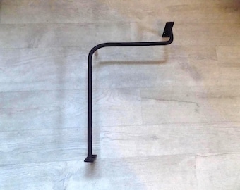 May include: A matte black metal L-shaped bracket featuring a curved corner and two flat mounting plates at each end. The structure is composed of a single continuous rod bent into a right angle, designed for wall or surface attachment.