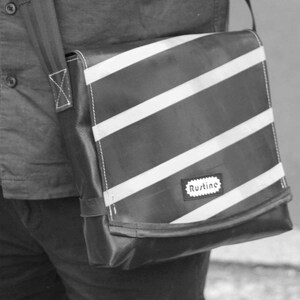 May include: A black and white striped messenger bag with a black strap and a white label that says "Rustine".